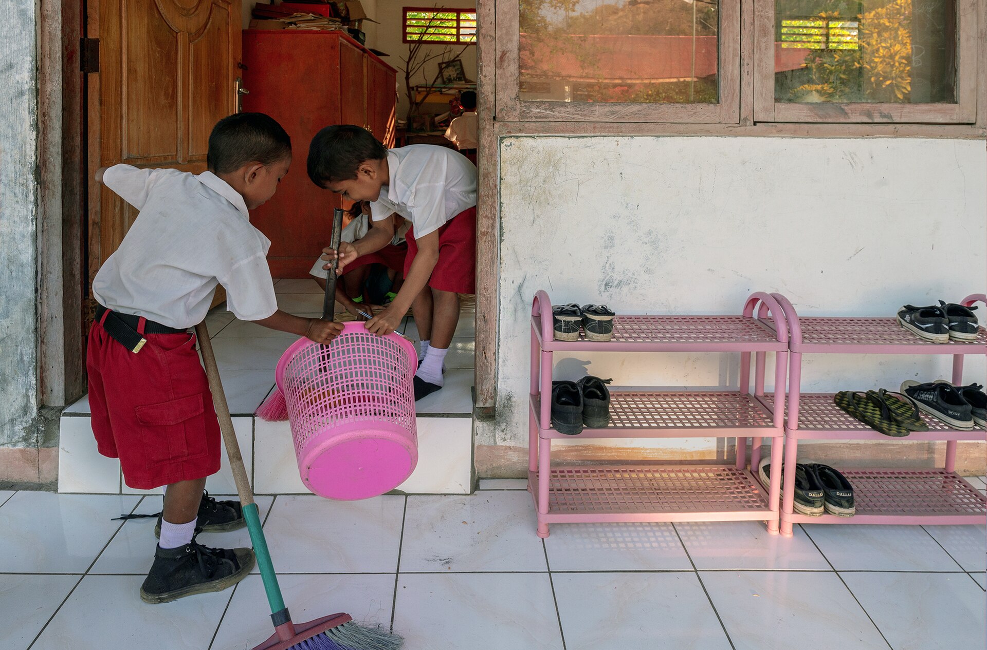 Two students in school uniforms sweep and collect trash outside, demonstrating community wellbeing.